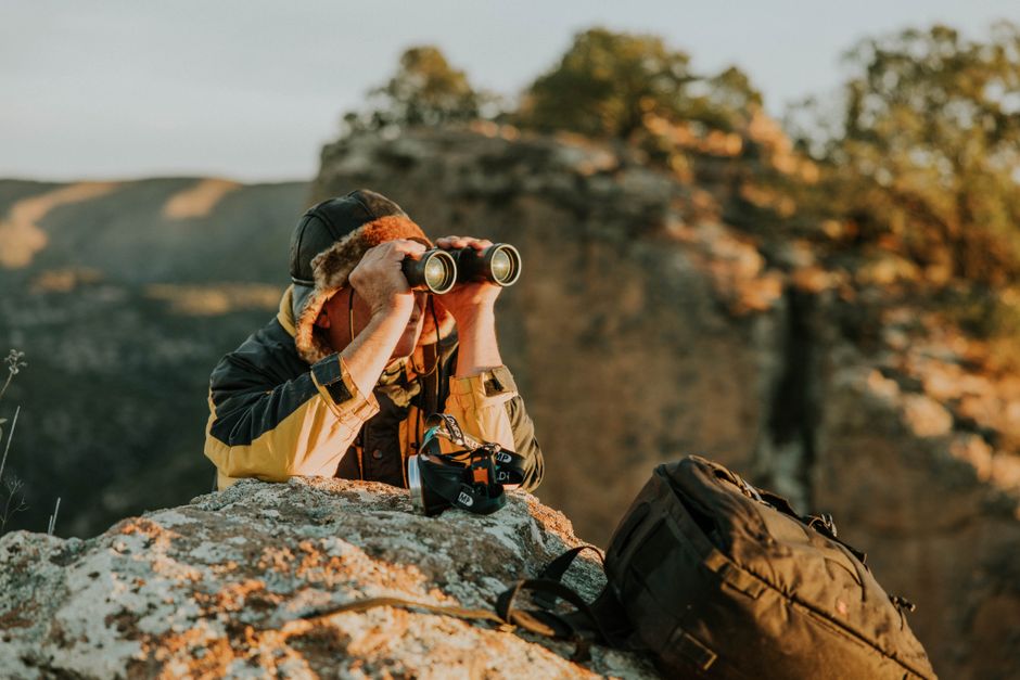 An adventurer observes through binoculars in a picturesque canyon landscape during dusk.